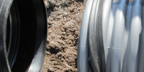 Dirt background in a ditch with a rubber gasket being pulled over a ribbed pipe