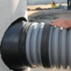 Gray ribbed pipe being inserted into a rubber connector on a manhole